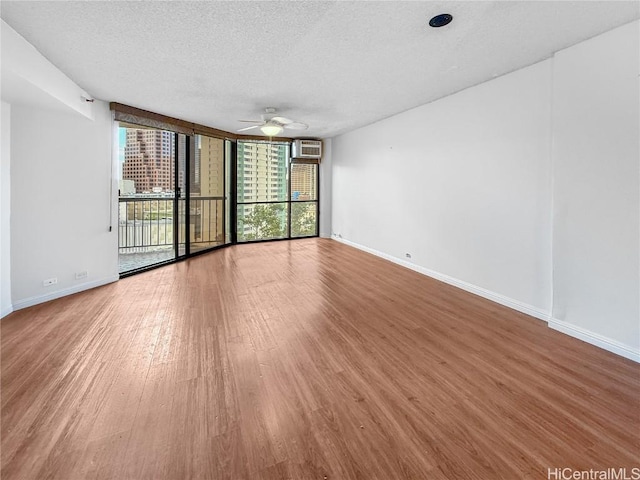 empty room with expansive windows, a textured ceiling, baseboards, and wood finished floors