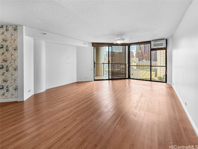 unfurnished room featuring ceiling fan, a textured ceiling, wood finished floors, baseboards, and expansive windows