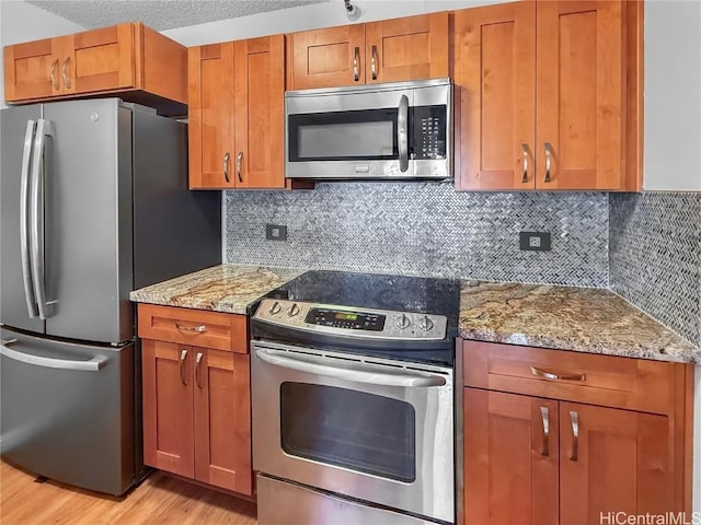 kitchen with stainless steel appliances, brown cabinets, light wood-style flooring, and light stone counters