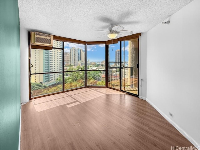 unfurnished sunroom featuring a view of city, a wall mounted air conditioner, and a ceiling fan