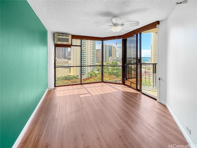 unfurnished sunroom with an AC wall unit, a city view, plenty of natural light, and ceiling fan