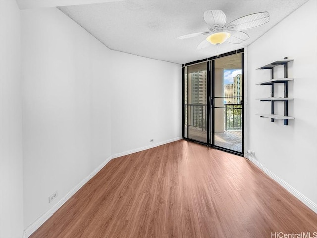 spare room with a wall of windows, a ceiling fan, baseboards, and wood finished floors