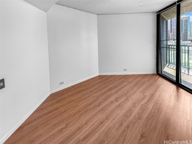 empty room with baseboards, a wall of windows, a textured ceiling, and light wood-style floors