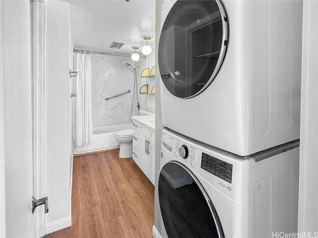 laundry room featuring light wood-type flooring, stacked washer and clothes dryer, and visible vents