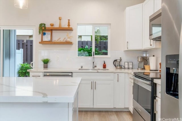 kitchen featuring backsplash, appliances with stainless steel finishes, white cabinetry, a sink, and light stone countertops