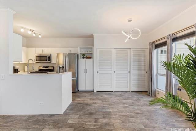 kitchen with wood finished floors, stainless steel appliances, white cabinets, crown molding, and hanging light fixtures