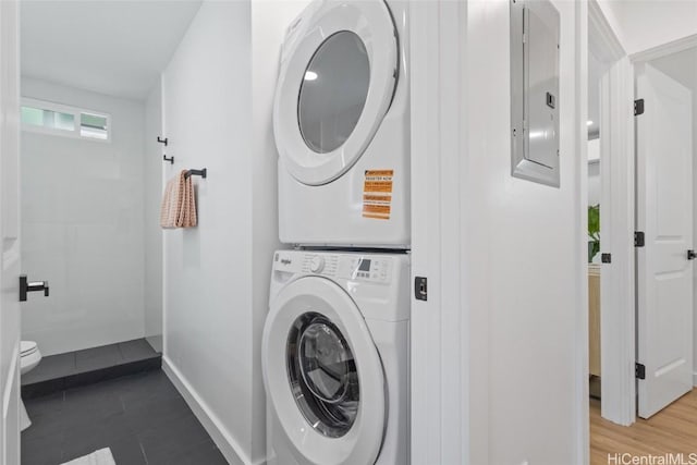 clothes washing area featuring stacked washer and clothes dryer, electric panel, baseboards, and laundry area