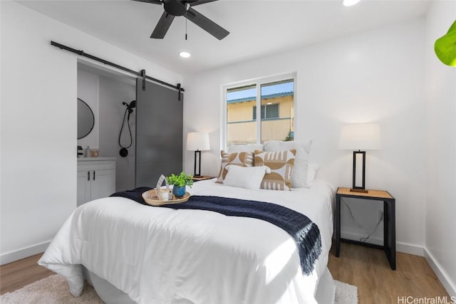 bedroom featuring recessed lighting, a barn door, a ceiling fan, wood finished floors, and baseboards