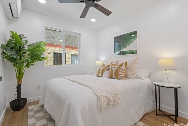 bedroom with a wall unit AC, recessed lighting, ceiling fan, wood finished floors, and baseboards