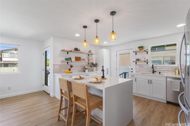 kitchen with light wood-style flooring, appliances with stainless steel finishes, light countertops, open shelves, and a sink