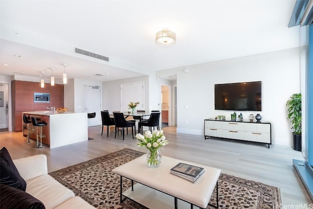 living room with light wood-type flooring, visible vents, and baseboards