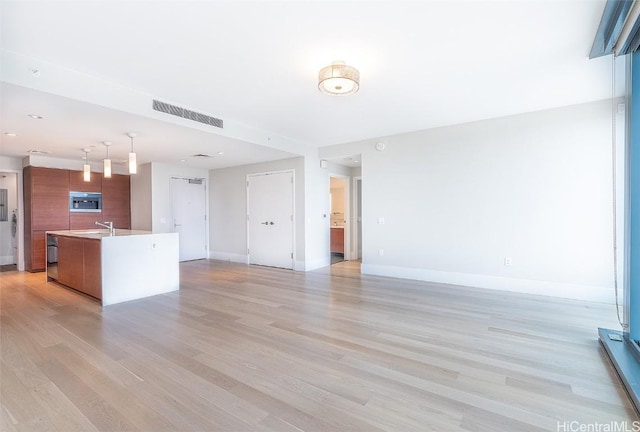 unfurnished living room with baseboards, a sink, visible vents, and light wood-style floors