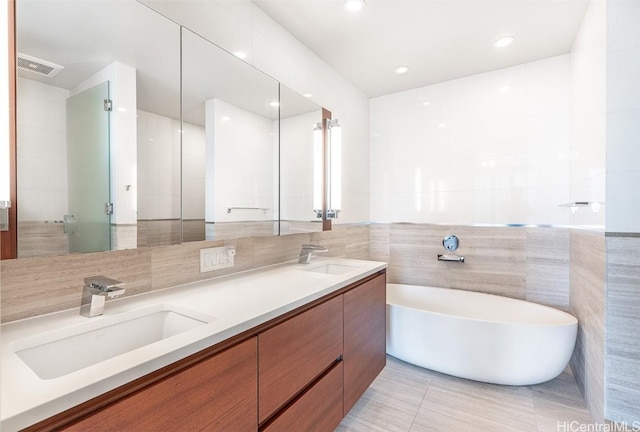 full bathroom featuring visible vents, a soaking tub, a sink, and tile walls