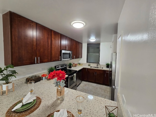 kitchen featuring light stone countertops, stainless steel appliances, and a sink