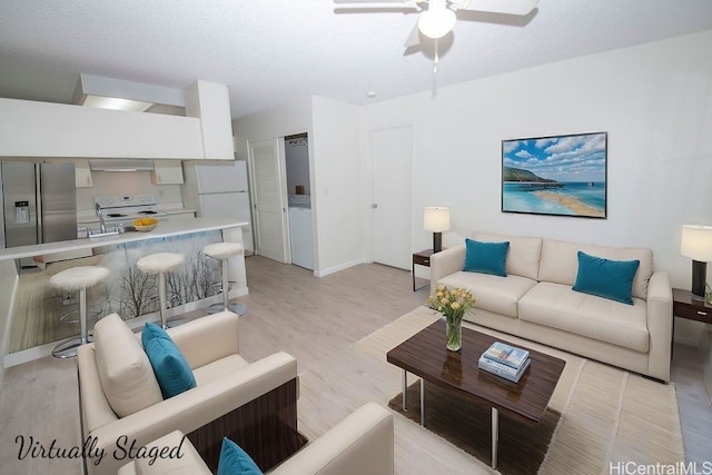 living room featuring light wood-type flooring, a textured ceiling, baseboards, and a ceiling fan