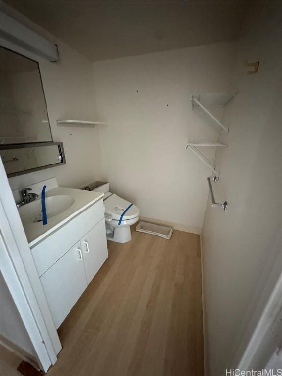 half bathroom featuring toilet, wood finished floors, and vanity