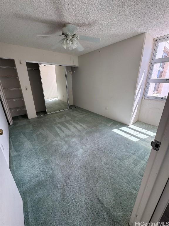 unfurnished bedroom with a textured ceiling, carpet flooring, two closets, and a ceiling fan