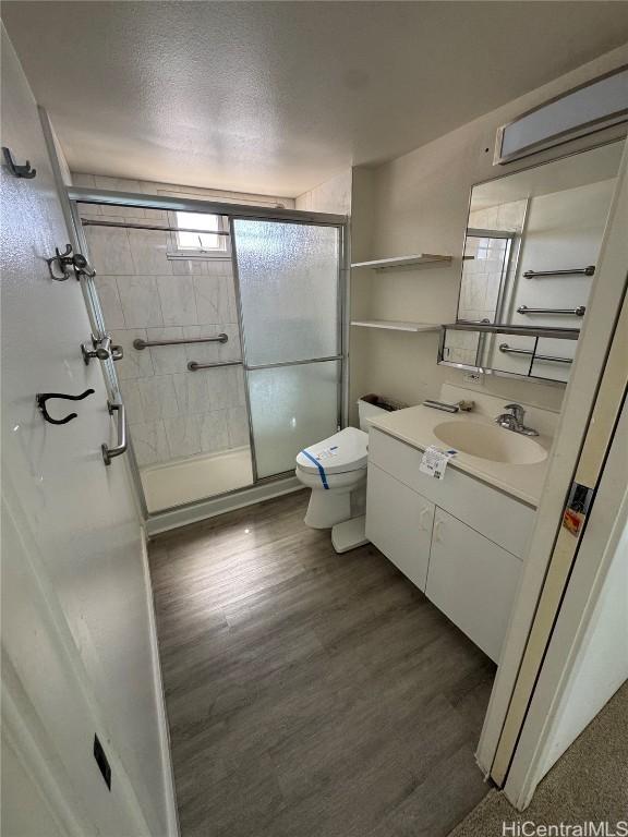 bathroom featuring a stall shower, toilet, wood finished floors, a textured ceiling, and vanity