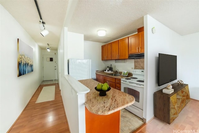 kitchen with brown cabinets, under cabinet range hood, a sink, a textured ceiling, and white range with electric stovetop