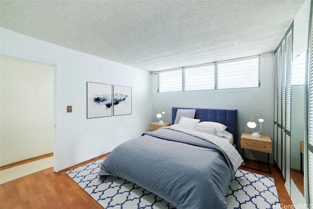 bedroom with a textured ceiling, concrete block wall, baseboards, and wood finished floors