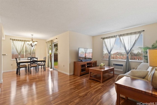 living room featuring a chandelier, a textured ceiling, wood finished floors, baseboards, and an AC wall unit