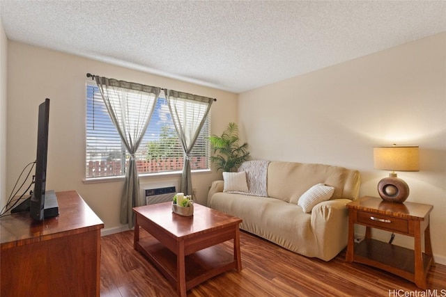 living room featuring an AC wall unit, a textured ceiling, baseboards, and wood finished floors