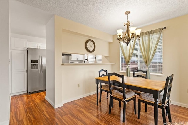 dining space featuring dark wood-type flooring, a textured ceiling, baseboards, and an inviting chandelier