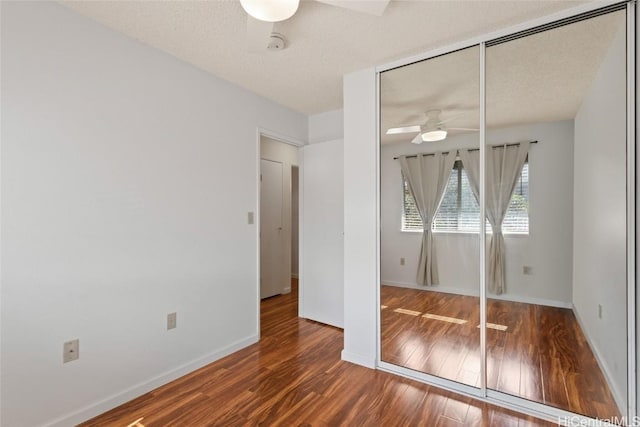 unfurnished bedroom featuring a textured ceiling, a closet, wood finished floors, and baseboards