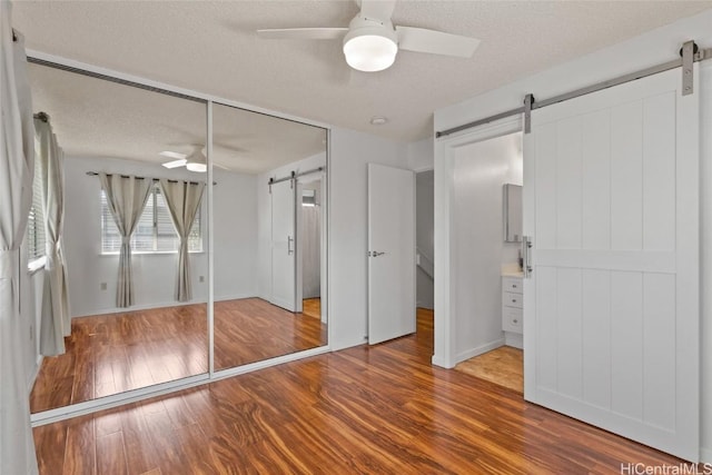 unfurnished bedroom featuring a ceiling fan, wood finished floors, a textured ceiling, and a barn door