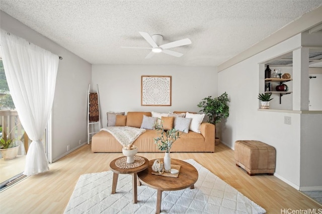 living area featuring light wood-type flooring, baseboards, a textured ceiling, and ceiling fan