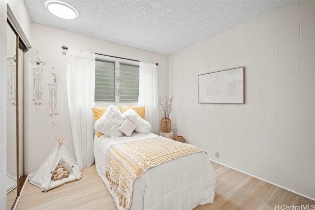 bedroom with a textured ceiling, wood finished floors, and concrete block wall