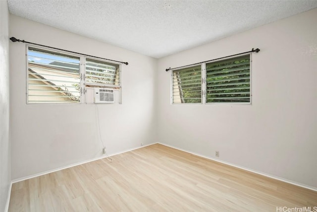 spare room featuring light wood finished floors, cooling unit, and a textured ceiling