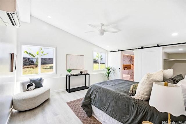 bedroom with light wood-style flooring, a barn door, connected bathroom, vaulted ceiling, and a wall mounted air conditioner