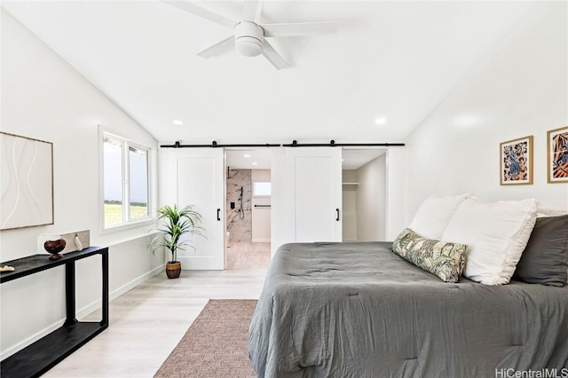 bedroom with a barn door, baseboards, ensuite bathroom, vaulted ceiling, and light wood-style floors