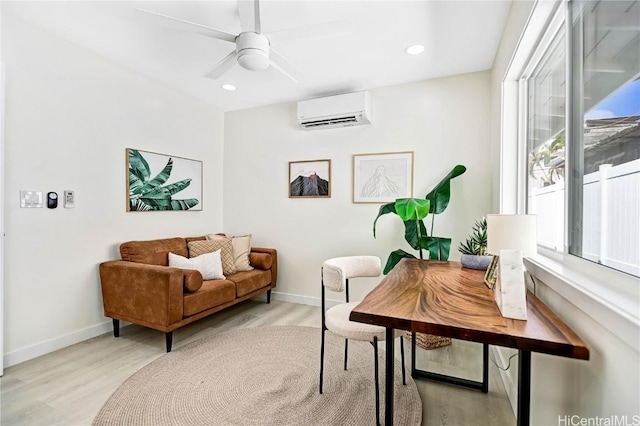 sitting room featuring a ceiling fan, a wall unit AC, light wood-style floors, and baseboards