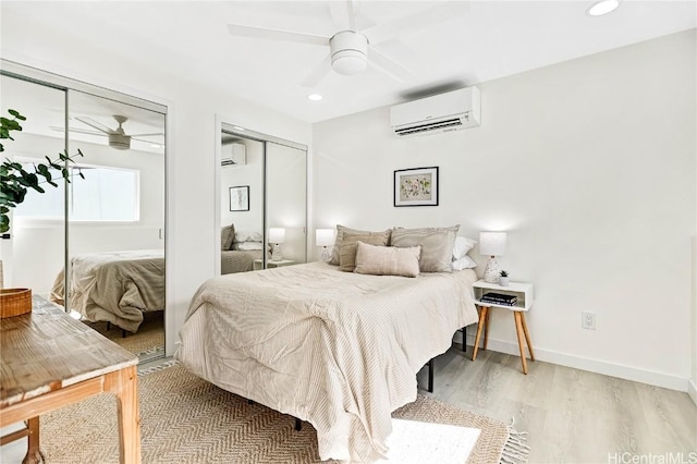 bedroom with baseboards, light wood finished floors, a wall unit AC, and multiple closets