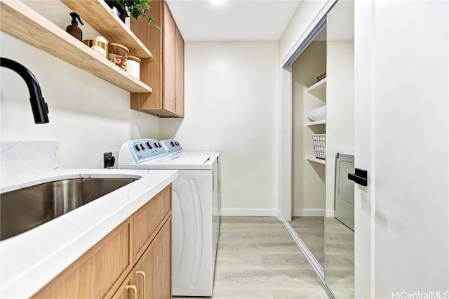 washroom featuring cabinet space, light wood-style floors, a sink, separate washer and dryer, and baseboards