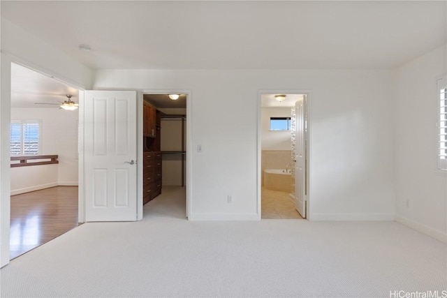 unfurnished bedroom with ensuite bathroom, baseboards, a walk in closet, and light colored carpet