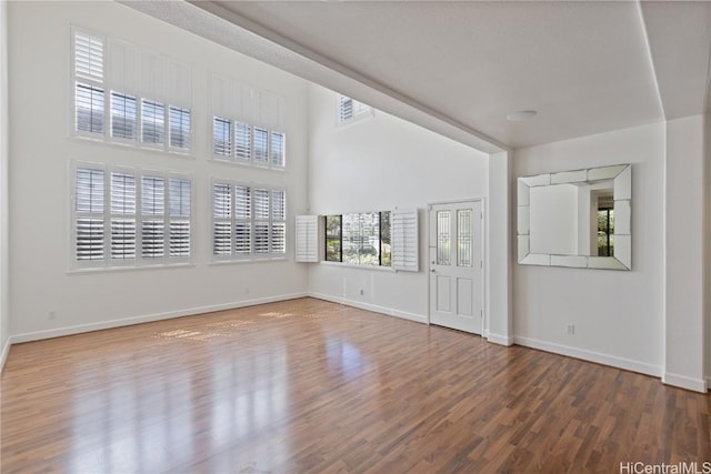 spare room featuring a towering ceiling, visible vents, baseboards, and wood finished floors