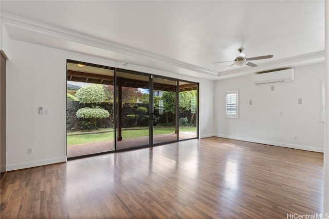 spare room featuring a tray ceiling, a wall mounted AC, wood finished floors, and baseboards