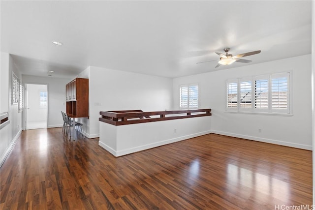 empty room with dark wood-style floors, a ceiling fan, and baseboards