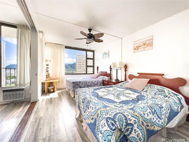 bedroom featuring a ceiling fan, an AC wall unit, multiple windows, and wood finished floors