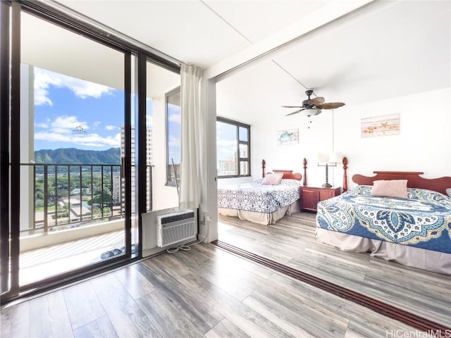 bedroom with a wall mounted AC, expansive windows, a mountain view, wood finished floors, and access to outside