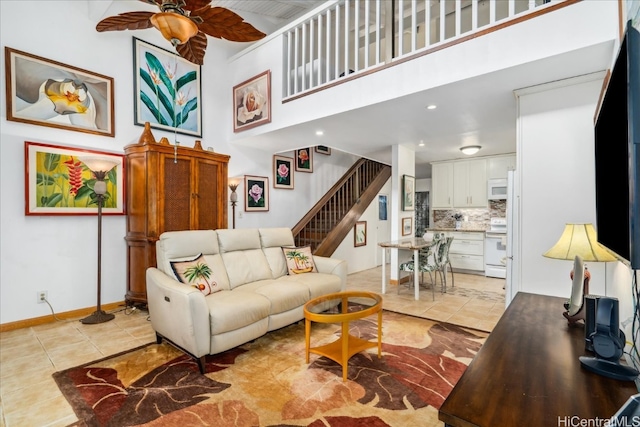 living room featuring a ceiling fan, light tile patterned flooring, stairway, and a high ceiling