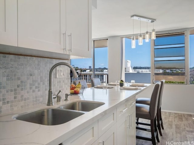 kitchen with light wood finished floors, tasteful backsplash, white cabinets, a sink, and light stone countertops