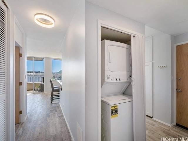 clothes washing area with stacked washer / drying machine, laundry area, light wood-style flooring, and baseboards