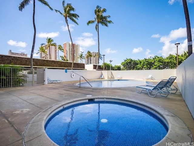 community pool featuring fence, a hot tub, and a patio