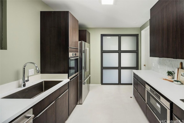 kitchen featuring dark brown cabinets, stainless steel appliances, light countertops, and a sink