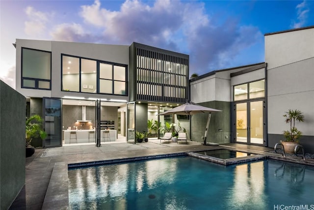 rear view of house with an outdoor pool, stucco siding, a patio, and an in ground hot tub