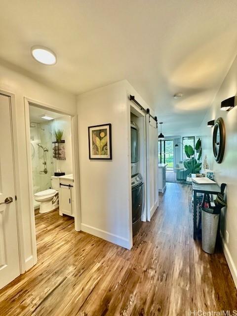 corridor with stacked washer and dryer, a barn door, baseboards, and wood finished floors